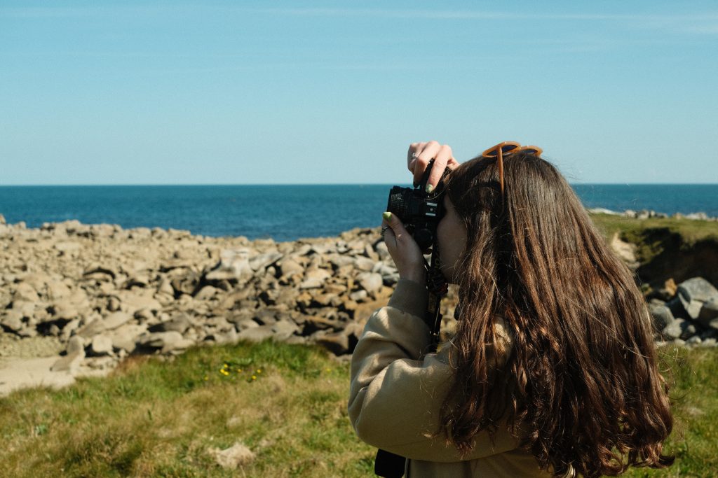 Photographe face à la mer sur la côte bretonne, appareil argentique à la main