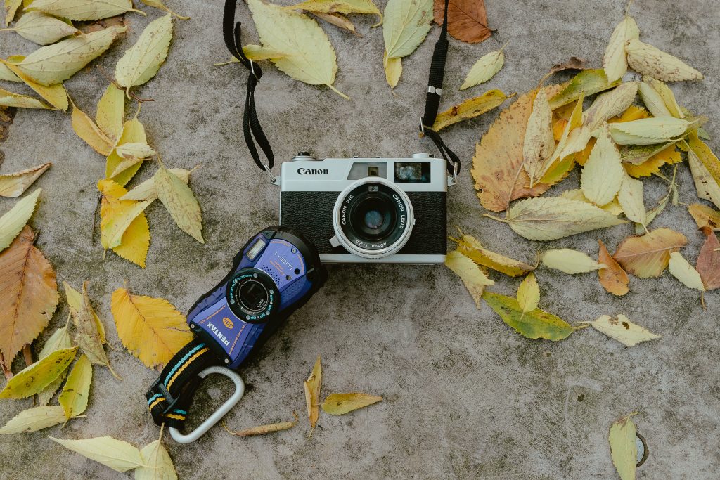 Un Canon argentique et un compact Pentax posés à plat sur du béton