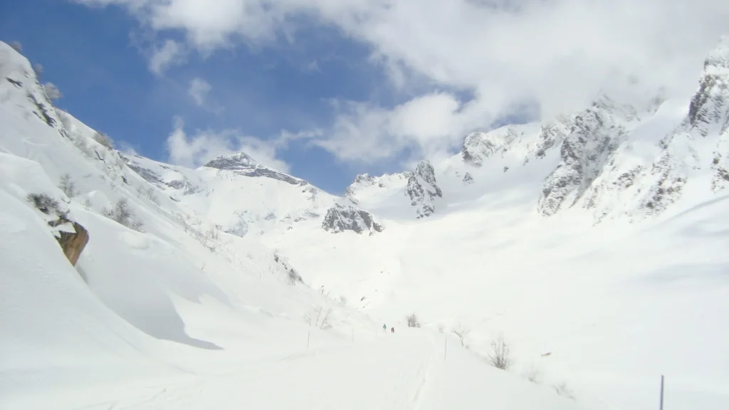 Une vallée enneigée avec un éperon rocheux à gauche, ciel bleu