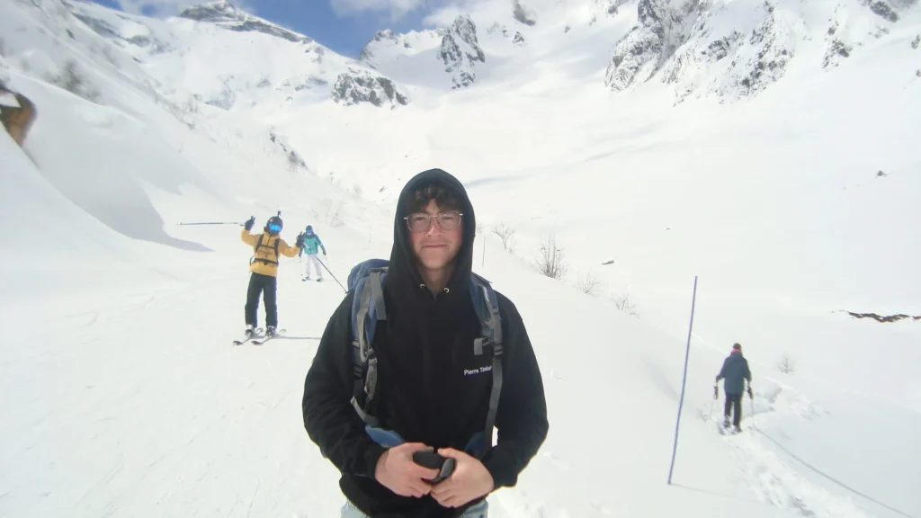 Un randonneur en veste noire face à l’objectif, marcheurs et skis derrière lui