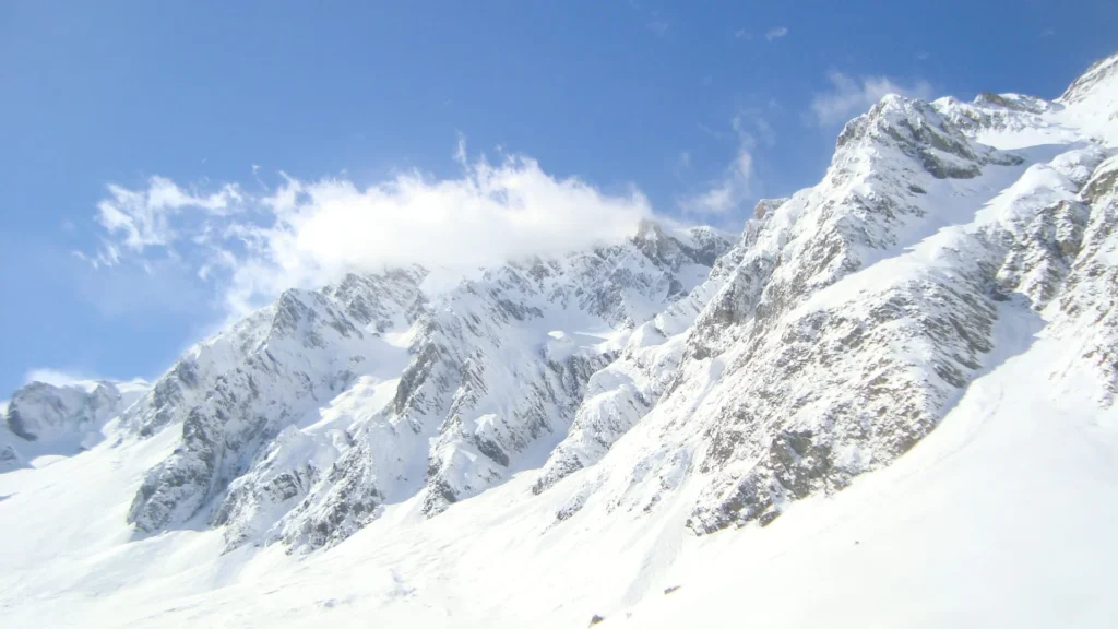 Une arête enneigée sous un ciel bleu nuageux, versant au soleil