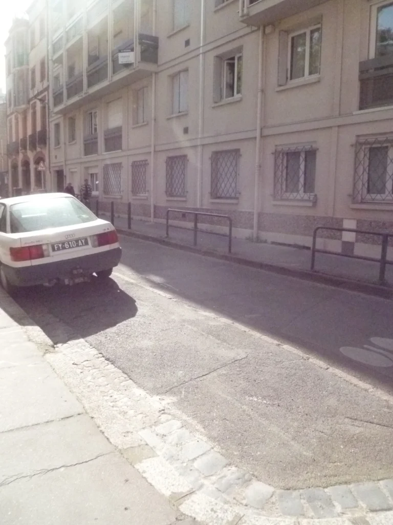 Une voiture blanche garée dans une rue étroite bordée d’immeubles
