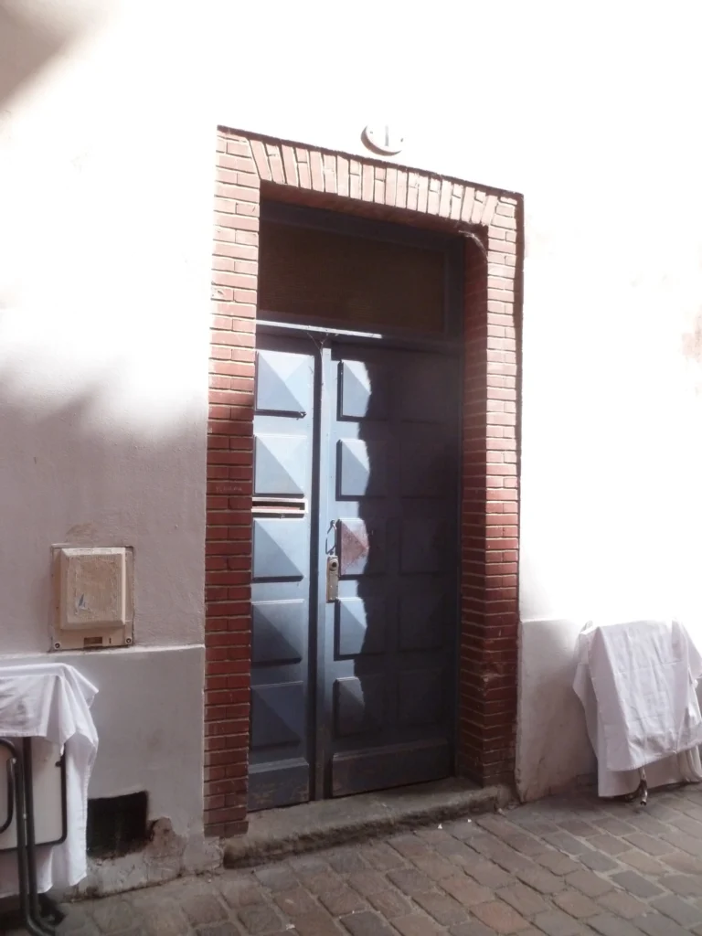 Détail d’une porte encadrée de brique et d’enduit blanc, ombre franche