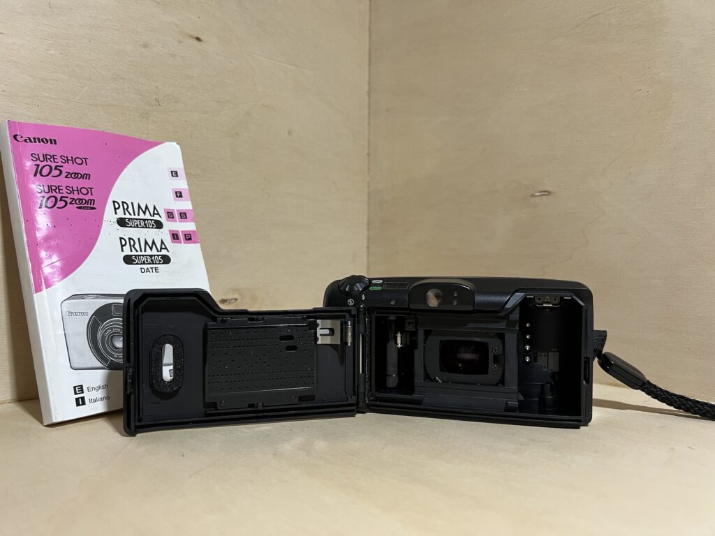Compact argentique ouvert sur l'atelier, chambre du film visible, notice d'origine posée à côté