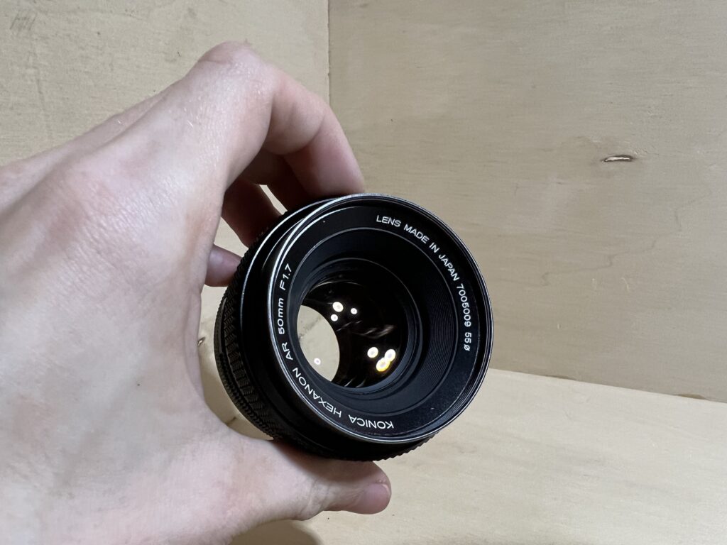 Lentille frontale d'un objectif Konica Hexanon inspectée en main, lamelles du diaphragme visibles