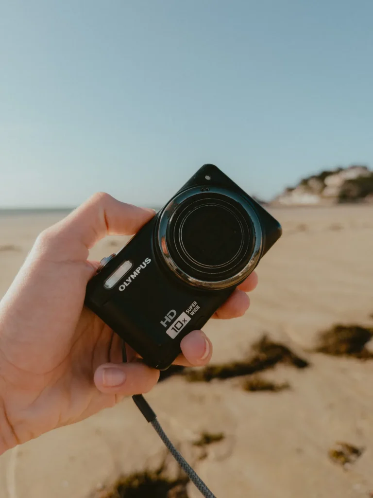 L’Olympus VR-310 tenu en main sur la plage, mention HD 10x Super Wide sur le boîtier