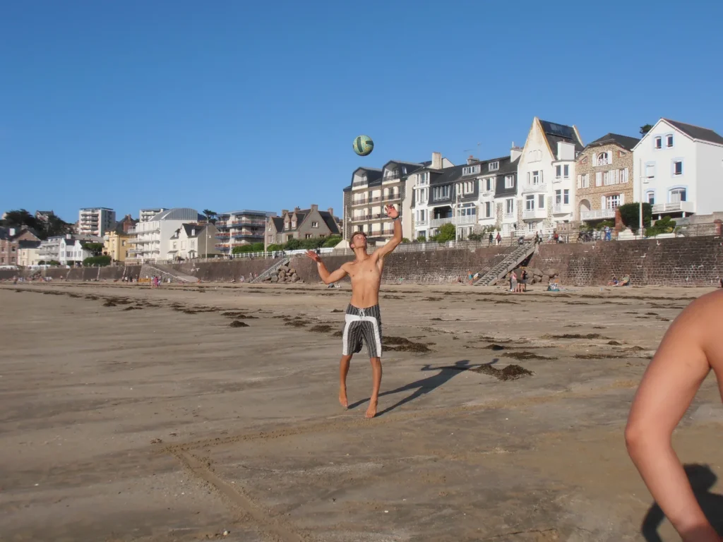 Un joueur au service, ballon en l’air devant les villas du front de mer